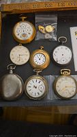Photo showing all six pocket watches arranged together with a bag of spare parts included.