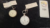 Two sterling silver pocket watches side by side with lot tag
