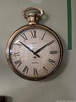Front view of United 8 Day wall clock with Roman numerals on cream face and brass case shaped like a pocket watch.