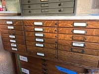Wooden oak parts cabinet with brass knobs and label holders; partial view of metal cabinet above