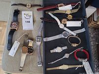 Overview of twelve wristwatches on cushion and in tray, six on left and six on right