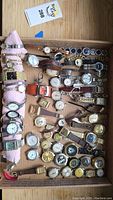 Overhead view of tray containing approximately 32 assorted wristwatches on a pink cloth roll and loose in a cardboard tray