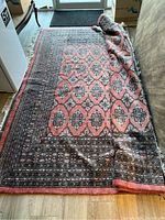 Rug partially unrolled on hardwood floor showing central coral pink and black geometric pattern.