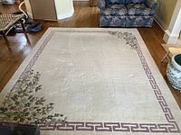 Full view of the large rectangular rug placed on hardwood floor with floral corner details and pink geometric border.