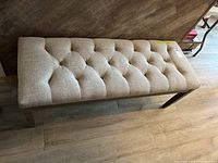 Top view of rectangular bench with beige tufted upholstery showing the seating surface and padding detail.