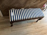 Top view of the wooden bench with blue and cream striped upholstery and MaxSold tag showing lot number.