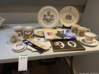 Various items laid out on a table showing plates, cups, framed photos, badges, and paper memorabilia