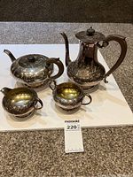 Full view of the four-piece Victorian tea and coffee set with engraved floral design sitting on a white board.