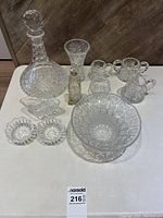 Full set of clear crystal and glass serveware on a white surface: decanter with stopper, vase, sugar bowl, creamer, medium bowl, small divided dish, round ribbed dishes.
