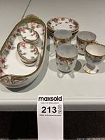 Image showing the entire set of porcelain serving ware items including rectangular tray, oval dishes, plates, cups, and goblet with floral patterns and gold edging.
