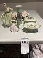 Photo showing two Doulton & Co. figurines, green vase, trinket box, soap dish, and decorative plates arranged on a table.