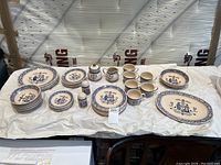 Overview photo of full set of Johnson Brothers dishes including plates, cups, sugar bowl, creamer, salt shaker and platters, arranged on white paper against wood background.