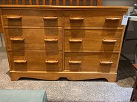 Front view of the maple wood dresser showing six drawers with wooden handles and scalloped base.