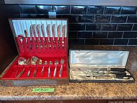 Image showing full flatware set in red velvet and white satin lined box next to stainless steel carving set in separate box on counter.