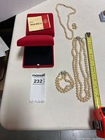 Full set displayed on table with measuring tape showing the length of necklaces, presentation box, paperwork, earrings, and bracelet.