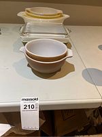 Set of Pyrex dishes including two mixing bowls, rectangular green floral baking dish with lid, and two white casserole dishes with yellow rims.