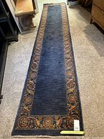 Full-length view showing navy blue central field with multicolor floral border and fringe at ends