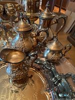 Photo showing teapot, sugar bowl, creamer, and large tray, all with ornate Victorian style silver plated design and some tarnish.