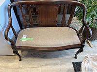 Full front view of wood framed settee with beige fabric seat upholstery showcasing curved arms and decorative detailing on backrest.