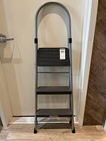 Front view of the silver metal frame step ladder with three black plastic steps and rounded top handle.