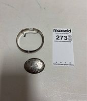 Top-down photo showing both the sterling silver bangle bracelet and the oval brooch with etched patterns and tarnish.