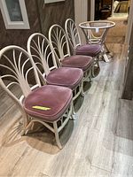 Four chairs with light-colored wooden frames, curved arch backs and dusty rose velvet cushions arranged in a row next to a matching round table base without glass top visible.
