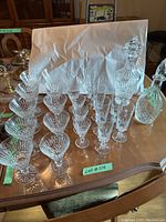 Group of cut crystal drinkware including eight wide bowl wine glasses, four slender champagne flutes, two decanters on wood table