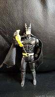 Front view of 1989 Toy Biz Batman action figure holding yellow retractable rope attached to utility belt against black background.