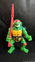Front view of 1991 Raphael Ninja Turtles figure holding red sai weapon with green body and red bandana.