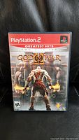 Front cover of God of War II PS2 Greatest Hits video game showing Kratos character in battle scene and official logos.