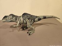 Side view of the gray and black camo patterned Giganotosaurus figure with textured skin and black claws, positioned on a flat surface.