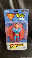 Front view of the sealed NECA Superman Toony Comics figure in original packaging showing the figure from chest up with a comic burst background.