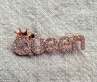 Front view of gold-tone metal brooch spelling "Queen" with clear rhinestones and crown detail on letter Q.