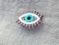 Front view of the gold-tone evil-eye pin brooch with rhinestones and enamel colors white, turquoise, and black, showing detailed decoration and size.