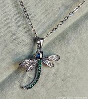 Close-up image of the dragonfly pendant showing the silver wings with diamond chips and green gemstone tail.