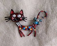 Front view of whimsical enamel cat brooch with red body, multicolored spots, rhinestone accents, and cartoon facial features.