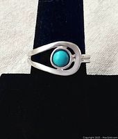 Front view of the silver ring with a round turquoise stone centered in an open teardrop silver setting, displayed on black ring holder.