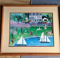 Photo of framed colorful folk art print depicting community scene with sailboats on pond and people walking and bicycling, signed by Regi Kleir.