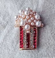 Close-up image of gold-tone popcorn brooch with pearl 'popcorn' and red and clear rhinestones on the popcorn box portion.