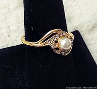 Front angle showing the pearl surrounded by rhinestones and gold-tone waved band.
