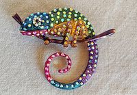 Front of chameleon brooch showing multicolored rhinestones, enamel details, and gold-tone branch.