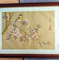 Full view of the framed silk painting depicting a bird and flowers on a silk cream-gold colored textured background with an Asian signature and red stamp.