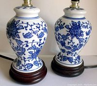 Pair of small boudoir lamps with blue and white porcelain bodies with floral designs on dark wooden bases shown upright.