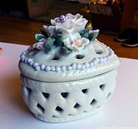 Angle view of the closed heart-shaped porcelain box with handcrafted flowers on the lid and pierced heart cutouts on the sides.