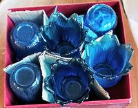 Top view of six blue glass tulip-shaped votive holders in original red box with cardboard dividers