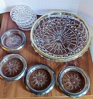 Overall view of vintage glass and crystal serving pieces with sterling silver trims including four sterling silver-rimmed coasters and four cut crystal coasters.