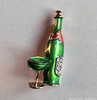 Front angle view showing green enamel wine bottle and glass brooch with gold-tone metal and rhinestone detail on bottle label