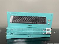 Three stacked turquoise boxes of Logitech K230 Bluetooth Keyboard, showing the side panel with model and product info.