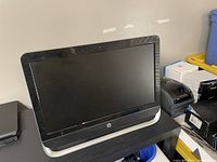 Front and side view of the HP Pavilion 23 All-in-One computer, showing the screen and base on a black table.