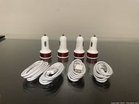 Four white USB car chargers with red metallic accents and four coiled white Apple Lightning cables displayed on a black surface.